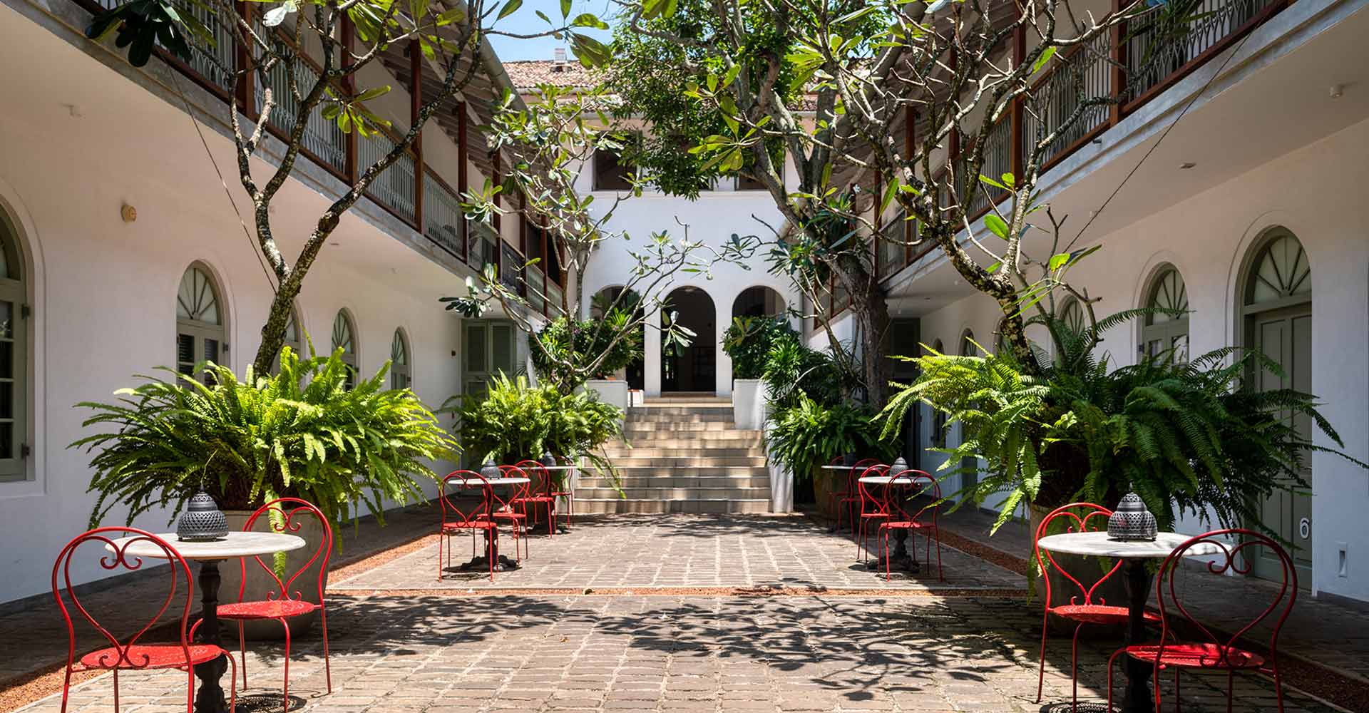 Fort Bazaar, a luxury boutique hotel in Galle, features a courtyard with red chairs, lush greenery, and colonial architecture