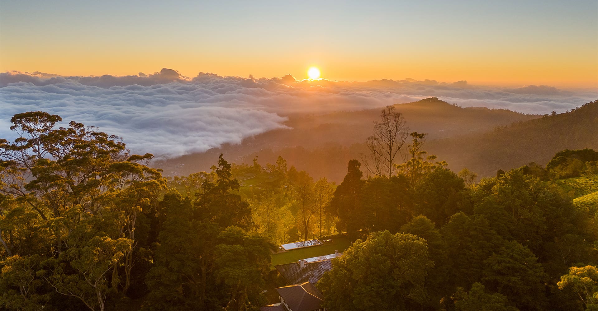 Stunning sunset view from Teardrop Hotels, a luxury boutique hotel in Sri Lanka, with mountains, clouds, and a distant hotel in the scene.